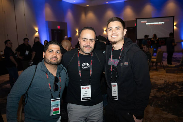 Three men smiling at the camera during an event with badges displayed.