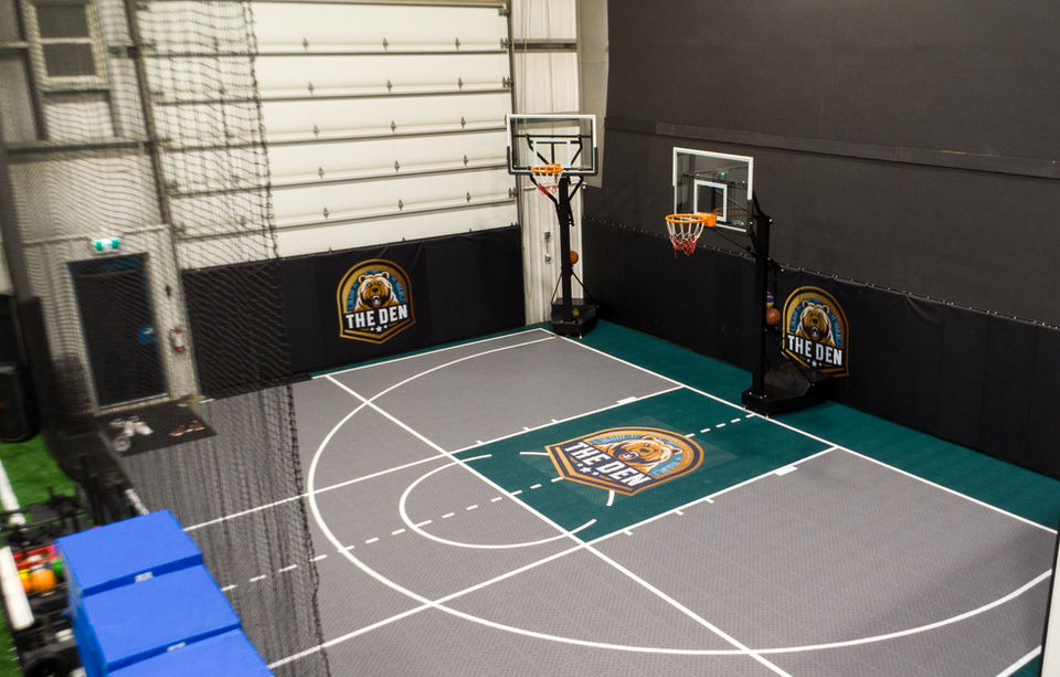 A basketball court with two hoops and The Den logo at the center.