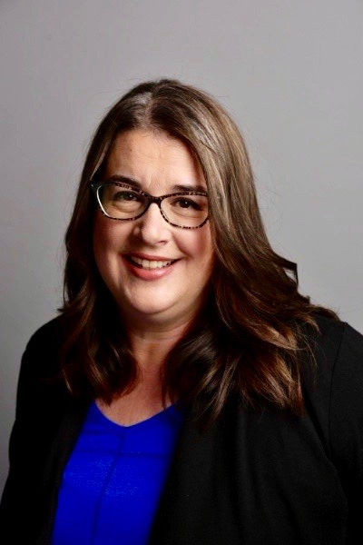 Smiling woman, with glasses, long dark hair, and a blue shirt