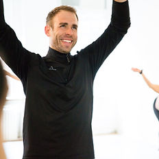 a man in an intenSati class is smiling and has his hands raised overhead