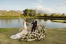 Bride and groom holding hands on their wedding ceremony platform surrounded by colourful flowers and Franschhoek