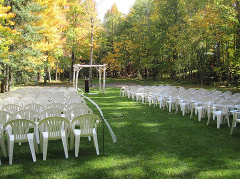 Outdoor wedding ceremony setup at Holiday Acres Resort with white chairs facing a rustic birch arch, surrounded by colorful fall foliage.
