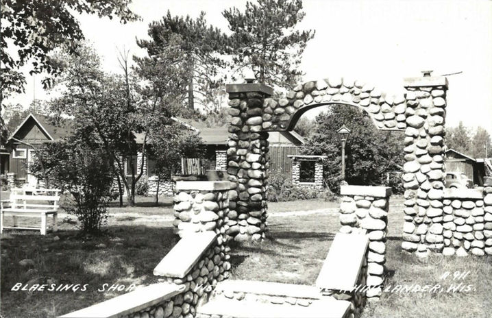 Vintage black and white photo showing stone archway with cabins and trees at Shorewood Vista in Rhinelander, Wisconsin.