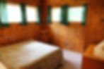 Double bed in pine-paneled room with green curtains in Cottage 22