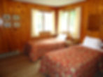 Bedroom with two twin beds covered in red floral quilts, wood-paneled walls, and large windows letting in natural light.