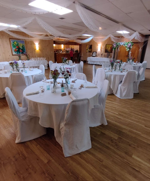 Indoor wedding reception hall at Holiday Acres Resort decorated with white linens, floral centerpieces, and ceiling draping for an elegant celebration.
