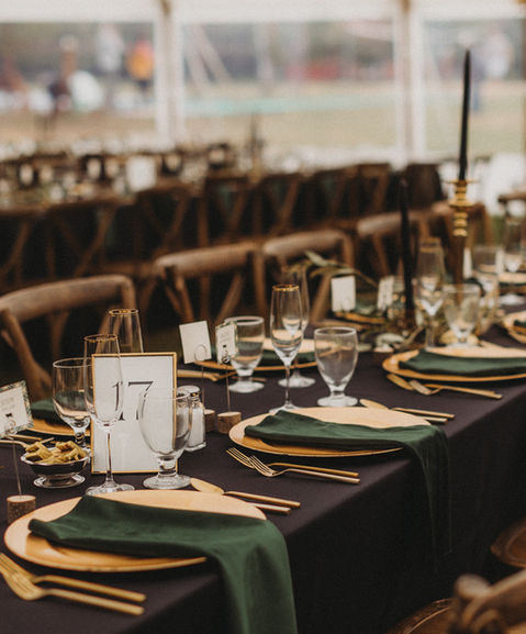 Elegant wedding reception table setting under a tent at Holiday Acres Resort, with gold chargers, green napkins, and wood chairs arranged for a formal dinner.