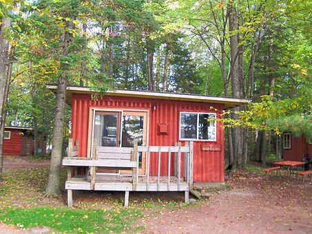 Rustic red cabin named Bob-O-Link with a small front porch, surrounded by tall trees and a picnic table nearby.