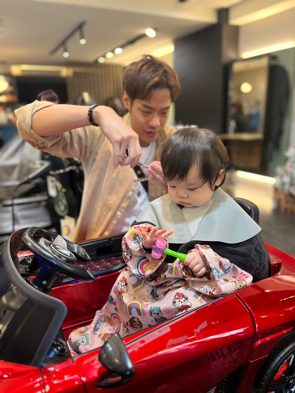 女童坐在紅色跑車椅中由設計師修剪頭髮並拿玩具安撫