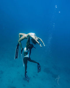 Woman in bikini held by diver underwater in deep blue ocean.
