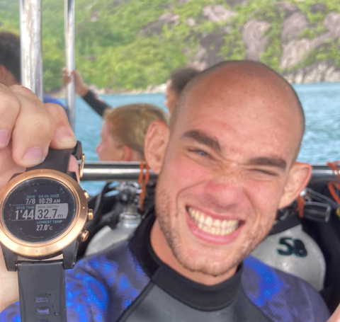 Smiling diver holds dive watch showing DIVE TIME 25M 24:26.