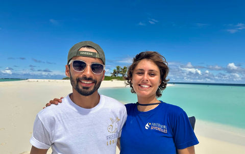 Smiling man and woman on pristine white sand beach, clear turquoise ocean.