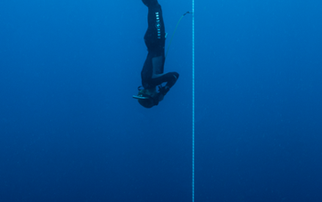 Freediver descending into deep blue ocean along a guide rope.
