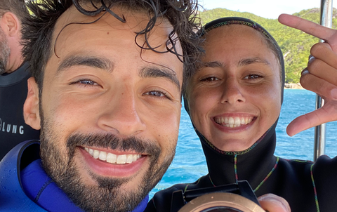 Smiling divers hold rose gold dive computer with 30.0 display, on boat.