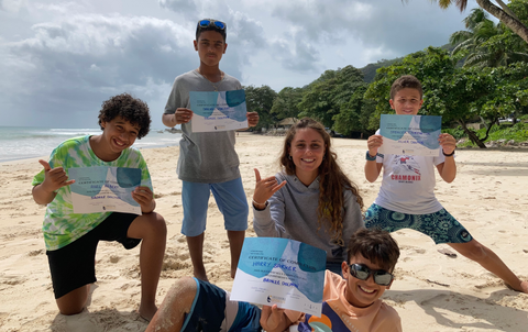 Five happy children display certificates on a sunny tropical beach.