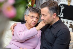 Middle aged man being comforted by an elderly woman, perhaps his mother. The first step in breaking the domestic violence cycle is to talk about it, and break the code of silence.