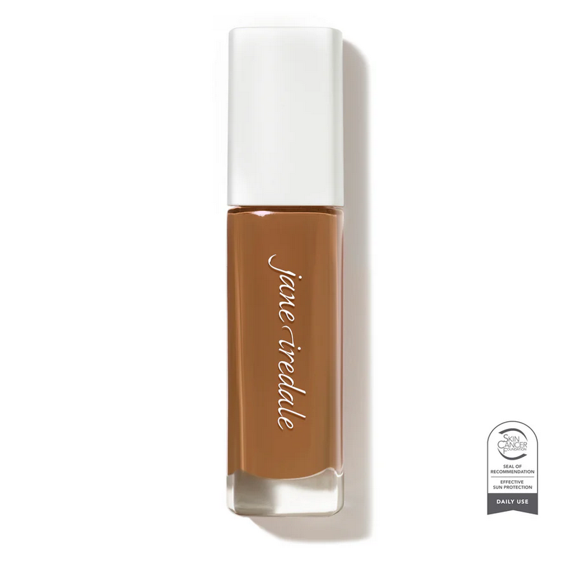 Clear glass make up bottle with a white top containing a dark face foundation.