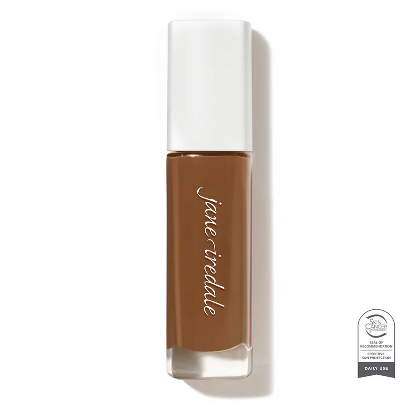 Clear glass make up bottle with a white top containing a dark face foundation.