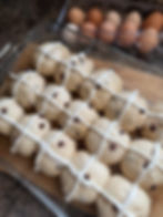 Chocolate chip buns with white icing in a glass tray, accompanied by brown and white eggs, on a wooden countertop.