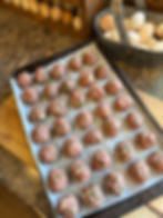 Tray of raw herb-flecked meatballs on parchment, with a metal bucket of eggs beside them on a kitchen counter.