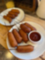 Corn dogs on a plate with a cup of ketchup, set on a wooden table, creating a cozy, appetizing mood.