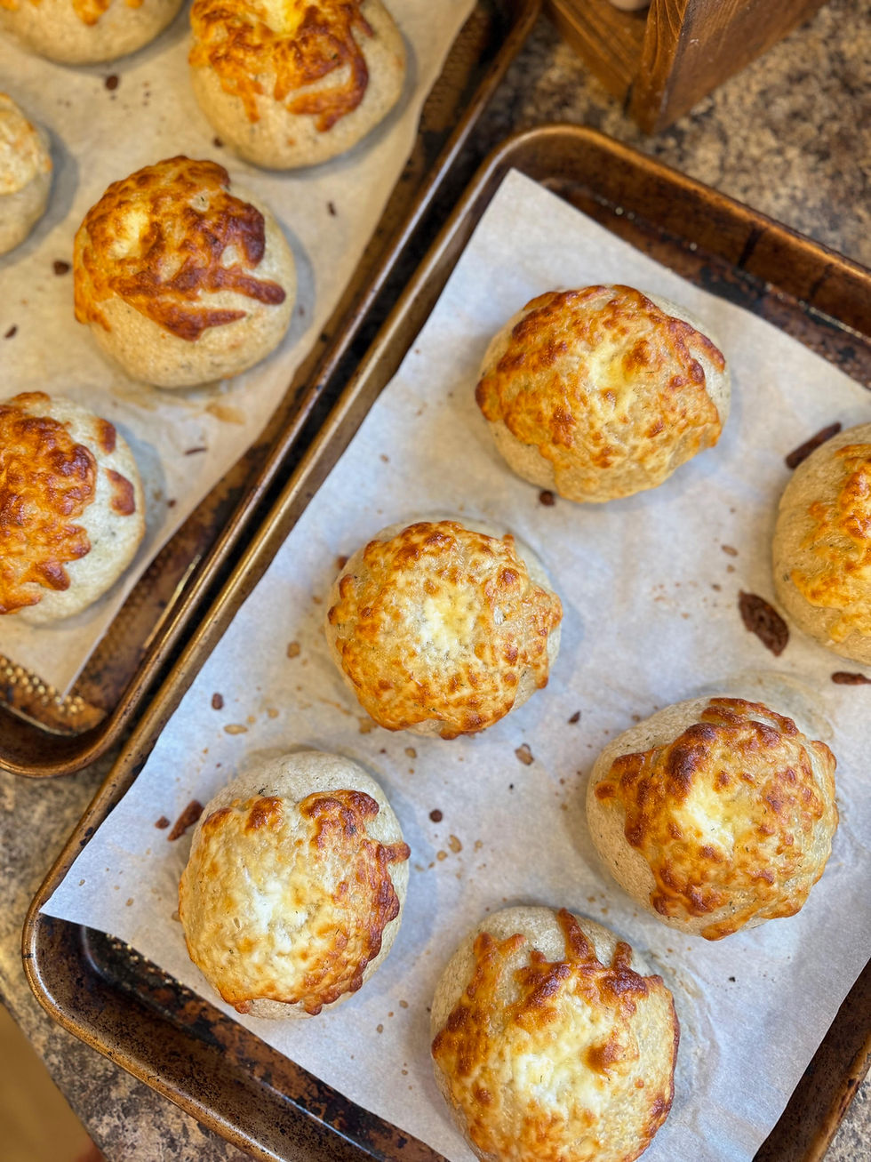 Golden cheese buns on parchment-lined baking sheets, resting on a rustic countertop. Warm, inviting colors. No visible text.