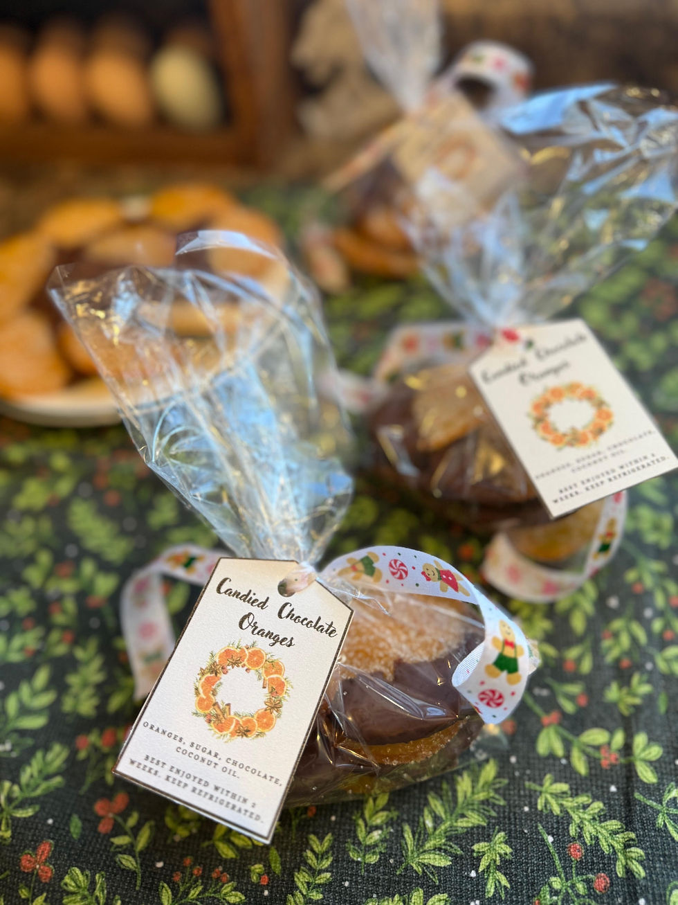 Bags of candied chocolate oranges with festive tags and ribbon on a green patterned cloth. Blurred background with cookies. Warm, cozy mood.