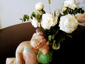 Une petite statuette du bouddha qui dort au pied d'un bouquet de pivoines blanches