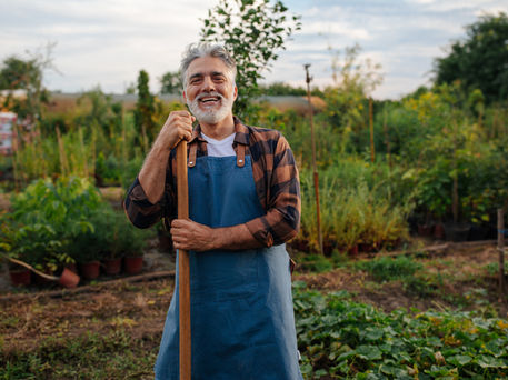 Proud elderly farmer smiling for the camera in his garden