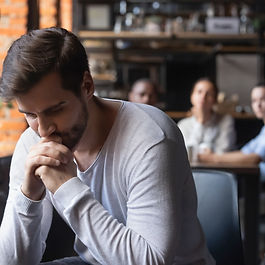 Guy sitting alone separately from other mates in cafe