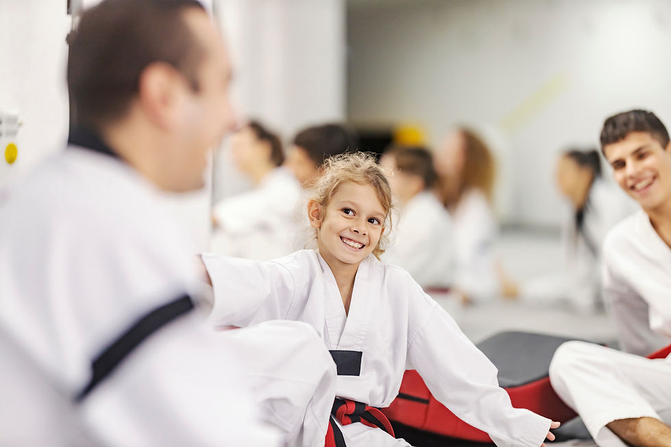 A little taekwondo athlete is sitting at martial art school with teammates and trainer and