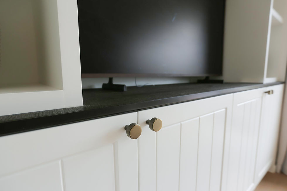 White cabinet with gold knobs beneath a black TV. The cabinet has paneled doors and open shelves, creating a modern, clean look.