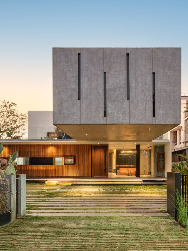 Modern house with concrete and wood facade, large windows, and green lawn in foreground. Clean lines, minimalist design, and serene mood.