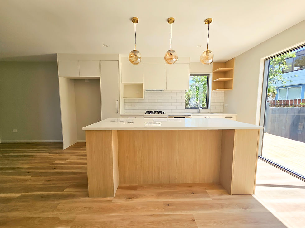 Modern kitchen with white cabinets, wooden island, and three pendant lights. Sunlit room with large window and wood floors. Minimalist design.