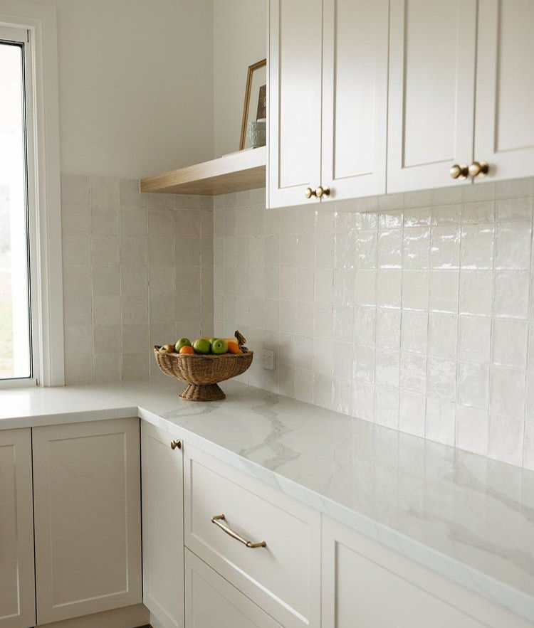 Bright kitchen with white cabinets and counter. A woven basket of fruit sits on the counter. Soft, natural light from a window.