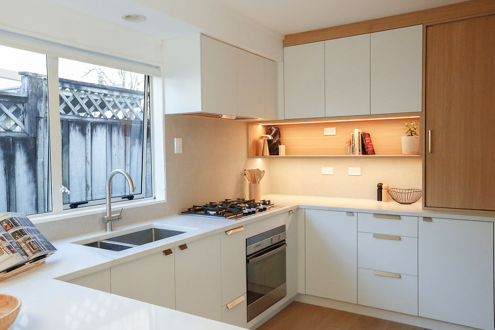 Modern kitchen with white cabinets, wood accents, a gas stove, and a sink by a window. Shelf with books and plant adds a cozy touch.