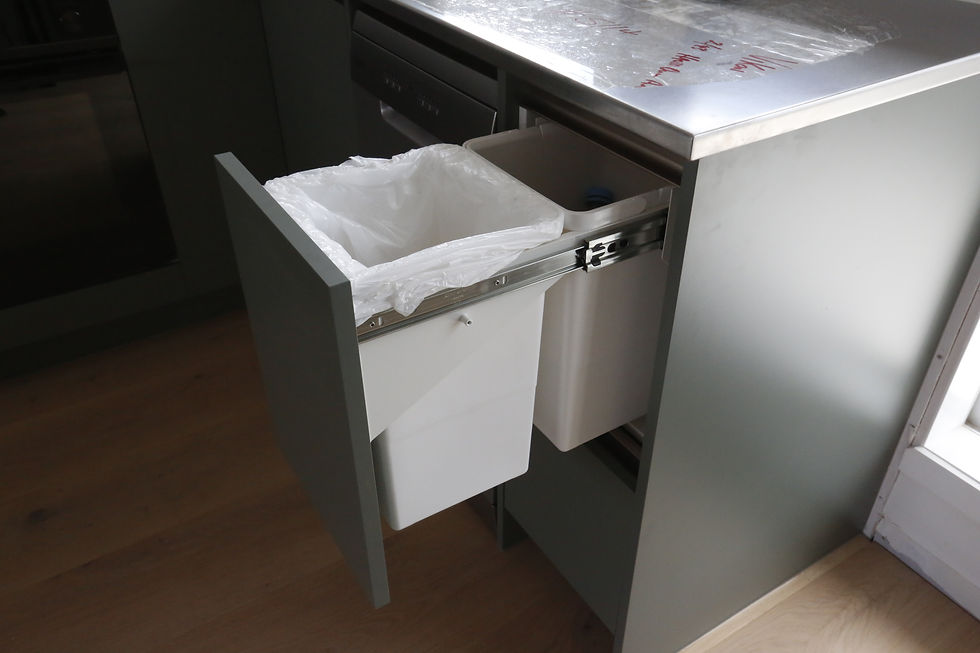 Pull-out kitchen drawer with two white trash bins, one open with a liner. Light gray cabinets and stainless steel countertop.