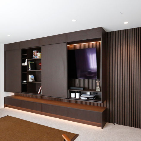 Full-wall entertainment unit with dark oak woodgrain cabinetry, warm LED lighting, and acoustic wall timber slatted panels