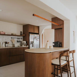 Modern kitchen with wooden cabinets, black countertops, and stainless steel appliances. Potted plant on counter. Bright, sleek ambiance.
