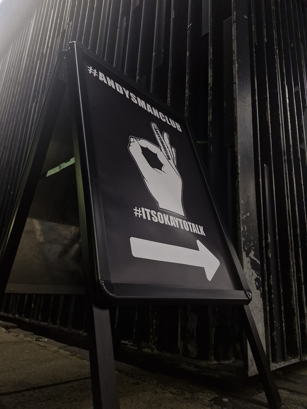 A standing sign outside of a local meeting spot of the club. The sign contains the Andys Man Club hand symbol of "ok"