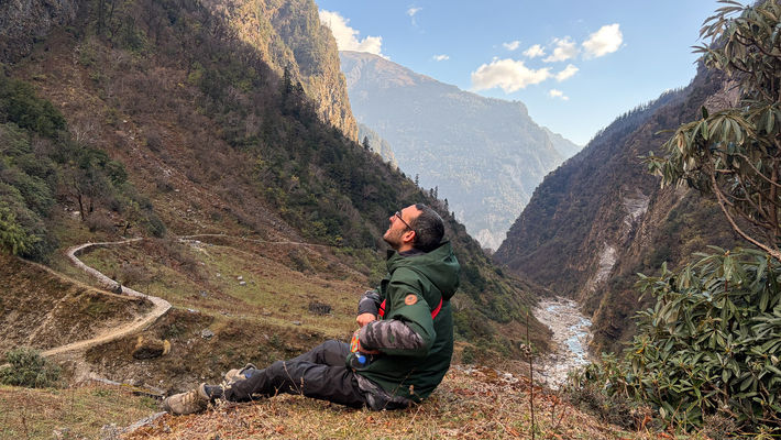 a hiker trying to spot a himalayan bird up in the sky while below him is flowing pindar river in the valley.