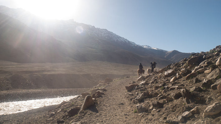 trekker and a horsemen meeting in the rough and rugged terrain of zanskar with bright sunshine .