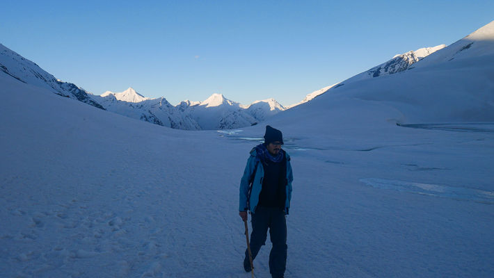 a trekker crossing white ice field on a high mountain pass in the Himalayas at the time of sunrise.