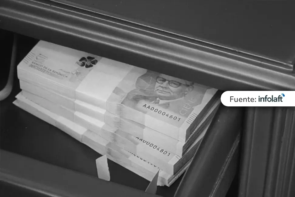 Fajo de billetes colombianos de cien mil pesos guardados en un cajón de madera.