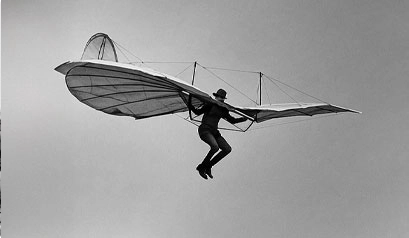 Inventor prueba un planeador primitivo con alas extendidas durante un vuelo experimental.