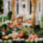 Layered autumn porch display with pumpkins, hay bales, cornstalks, and seasonal greenery