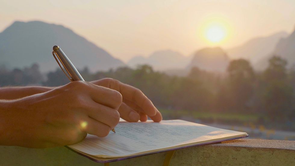Persona escribiendo en un cuaderno al amanecer, reflexionando al aire libre frente a un paisaje de montañas
