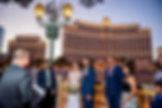 "Latino couple surrounded by loved ones listening to their bilingual wedding officiant in front of the Bellagio Hotel in Las Vegas