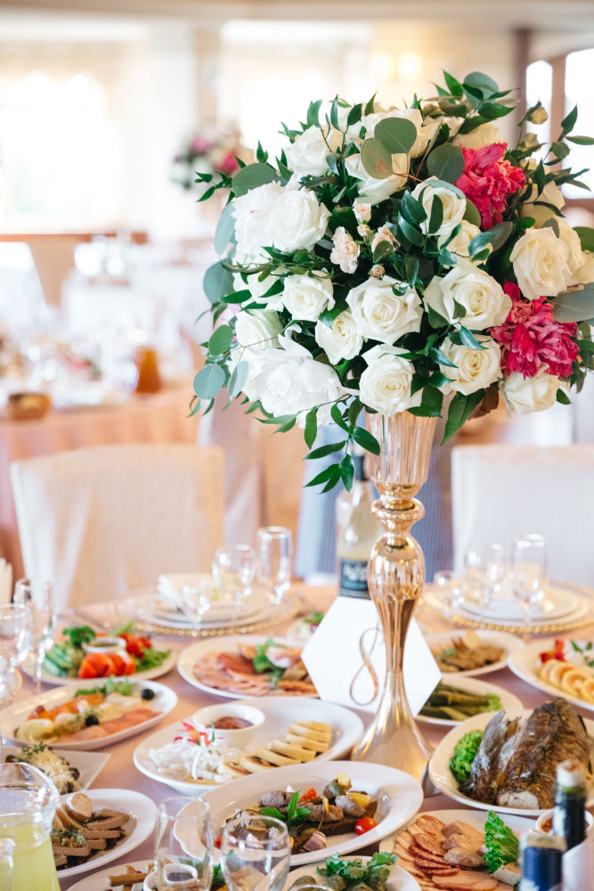 Centro de mesa de rosas blancas y rosas sobre una mesa con comida de la recepción de bodas