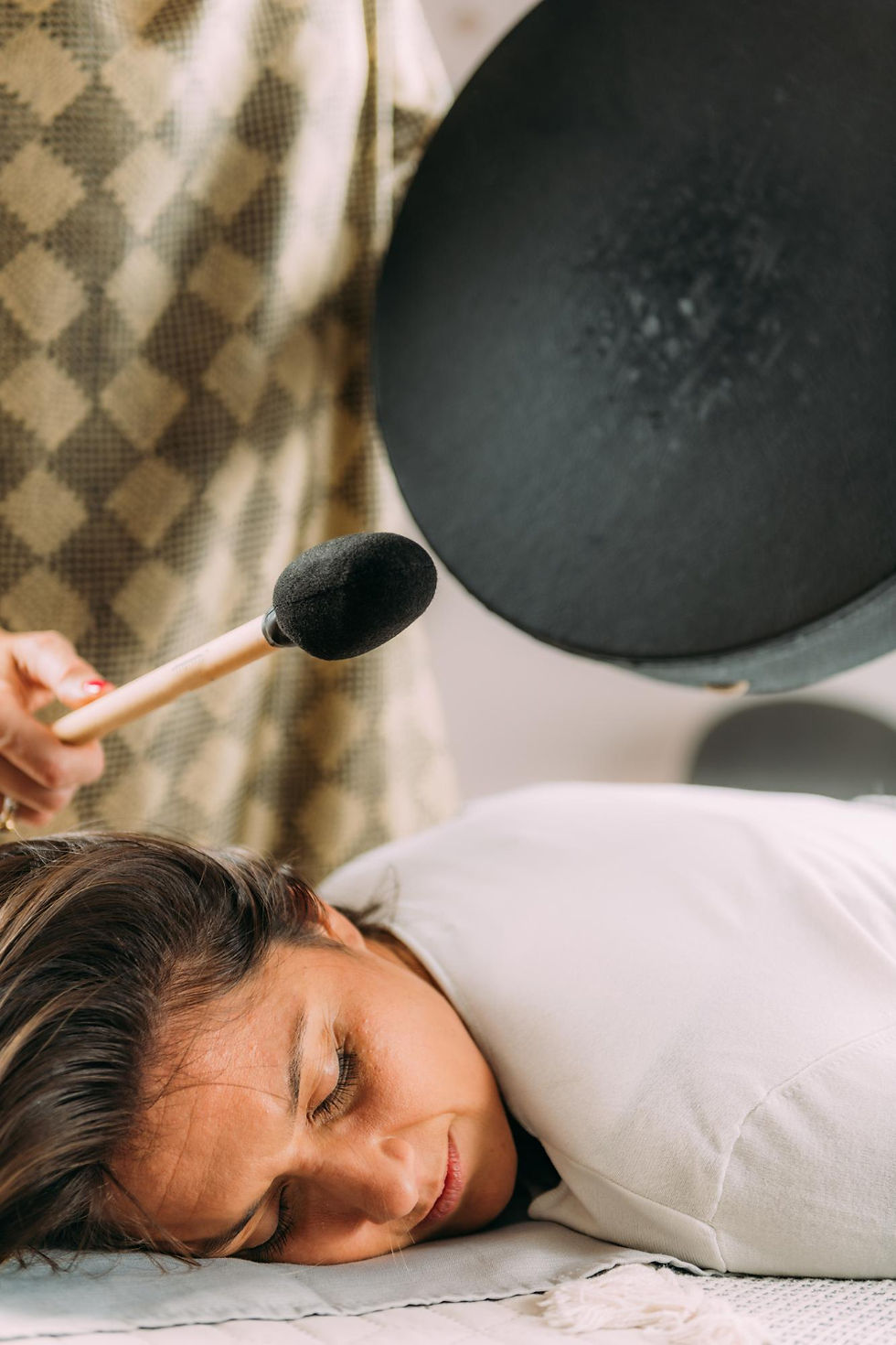 Relaxed woman lying face down receiving a healing sound therapy with a percussion instrument